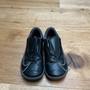 Svarta Nike Mercurial fotbollsskor - Säljer ett par svarta Nike Mercurial fotbollsskor med kardborreband. Skorna har en stilren design med vita detaljer och en slitstark sula. Perfekta för inomhusfotboll eller träning.