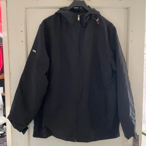 Svart jacka från Urban Spirit - Säljer en svart jacka från Urban Spirit i storlek L. Den har en enkel och stilren design med dragkedja framtill och en praktisk huva. Perfekt för höst- och vårsäsongen. Jackan är i bra skick och redo för nya äventyr!