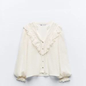 Vit blus med volangdetaljer - Säljer en superfin vit blus från Zara med volangdetaljer längs kragen och knappar framtill. Blusen har långa ärmar med elastiska muddar som ger en romantisk touch. Perfekt för både vardag och fest! Kom privat för fler bilder🤍💕🤍Endast använd en gång 
