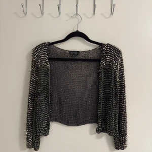 Glittrig kofta från Topshop - Säljer en superglittrig kofta från Topshop som är perfekt för festliga tillfällen. Den är täckt med paljetter och har en öppen design. Koftan är croppad och har långa ärmar. Perfekt för att lysa upp vilken outfit som helst! 