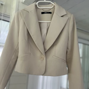 Beige kavaj från Gina Tricot - Säljer en superfin beige kavaj från Gina Tricot i storlek XS. Den är croppad och har en knapp framtill. Perfekt för både vardag och fest! 💫