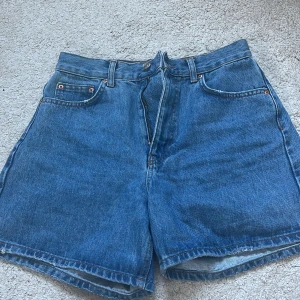 Blå jeansshorts från Gina Tricot - Säljer ett par klassiska blå jeansshorts från Gina Tricot i storlek 36. De är högmidjade med fem fickor och knappgylf. Perfekta för sommardagar eller en avslappnad stil 💙