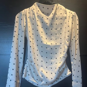 Blus - Satinblus med hög hals (ej åtsittande) och detaljer vid axlarna och sidorna.
