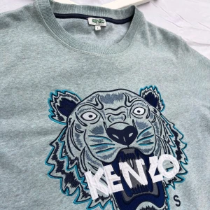 Kenzo tiger klassisk sweatshirt (sällsynt färg) ljusblå - Använd och väl omhändertagen. OBS! Den vita bakgrunden får plagget att se mörk och smutsig ut. ”En sällsynt färg” på den kända Kenzo tröjan med lejonet. Väldigt bekväm tröja med bra passform. Kvalite som man båda se och känner. Butikpris: 3200 kr 