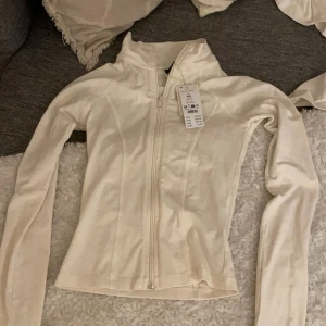 Vit långärmad jacka med dragkedja - Säljer min vit/beige soft touch zip jacket från Ginatricot i färgen tofu då den är för liten för mig. Den är helt ny och knappt använd, väldigt bra skick. 