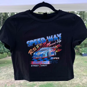 Croppad svart T-shirt  - En croppad svart t-shirt med färgglatt tryck ❤️💙 En aning liten i storleken då jag normalt har S i toppar. Sparsamt använd!  Längd: 41 cm Axel: 37 cm Byst: 80 cm