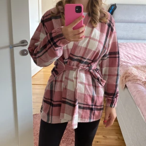 Rutig rosa och vit skjorta - Säljer en superfin rutig skjorta i rosa och vitt med svarta detaljer. koftan har långa ärmar och en knytning framtill som ger en snygg look. Perfekt för en avslappnad stil eller som ett extra lager under hösten. står M men känns mer som S.