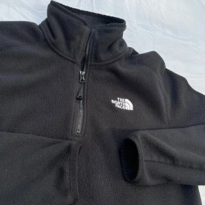 The North Face: half zip fleece svart - Använd och väl omhändertagen. Värmande fleecetröja med dragkedja i kragen från det amerikanska varumärket The North Face. Tillverkad av en mjuk polyester, ett plagg som andas och fungerar bra under jackan, kan bäras lager-på-lager. Butikpris: 700 kr