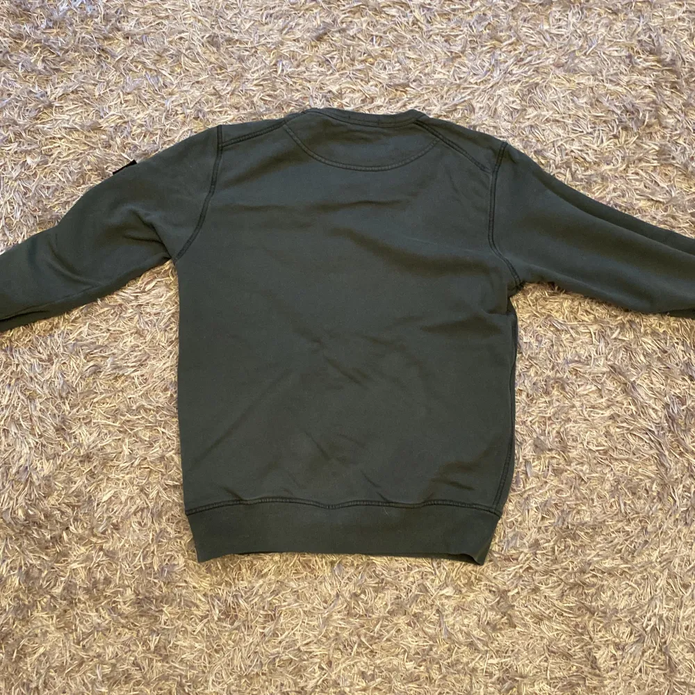 Säljer en snygg och stilren mörkgrön tröja från Stone Island. Den har långa ärmar och en klassisk rund halsringning. Tröjan är i bra skick och har det ikoniska Stone Island-märket på ärmen. Perfekt för höst och vinter!. Neuletakit & Villapaidat.