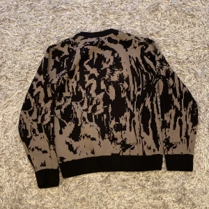 Mönstrad tröja från Weekday - Säljer en cool mönstrad tröja från Weekday i storlek XS. Tröjan har ett unikt svart och beige mönster som ger en edgy look. Den är perfekt för höst och vinter med sina långa ärmar och mjuka material. Passar både till vardags och fest!