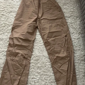 Beige cargopants - Säljer ett par beige parachute/cargopants i storlek S. Byxorna har en avslappnad och bekväm passform med elastisk midja och snörning för extra komfort. Perfekta för en casual look De har flera praktiska fickor för förvaring.