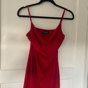 Röd klänning från Paradis London - Säljer en superfin röd klänning från Paradis London. Den har en elegant draperad framsida och smala axelband. Klänningen är dekorerad med spetsdetaljer längst ner. Klänningen är i väldigt bra skick!