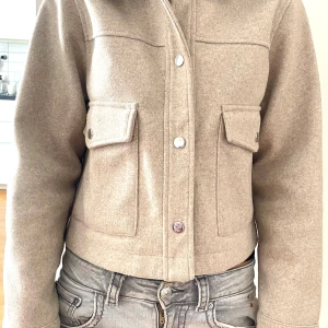 Beige jacka från Zara - Säljer en snygg beige jacka från Zara i storlek S. Jackan har en stilren design med knappar framtill och två praktiska fickor med lock. Perfekt för både vår och höst!
