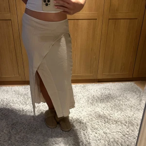Beige omlottkjol - Snygg beige omlottkjol med slits. Perfekt för en stilren look. Kjolen har en lång design och är lätt att matcha med olika toppar.