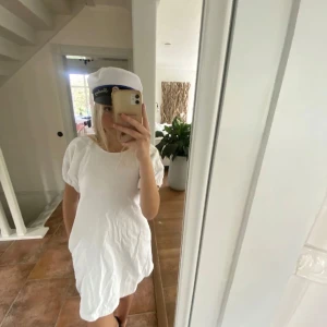Vit klänning - Säljer en söt vit klänning med korta ärmar och en fin öppen rygg med knytband. Helt oanvänd, passar perfekt för studenten, jeanstyg typ. Har diskreta fickor.