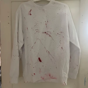 Vit tröja med färgstänk från H&M - Säljer en vit tröja från H&M med unika röda färgstänk. Tröjan har en avslappnad passform och långa ärmar. Perfekt för dig som vill ha något annorlunda i garderoben. 🖤