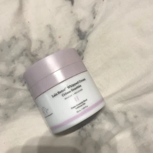 Lala Retro Whipped Cream från Drunk Elephant - En lyxig ansiktskräm från Drunk Elephant, Lala Retro Whipped Cream, i en stilren burk med ljust lila lock. Innehåller 50 ml och är designad för att återfukta och återställa huden med en rik och krämig konsistens.