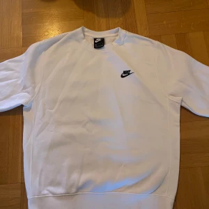 Vit sweatshirt från Nike - Säljer en stilren vit sweatshirt från Nike med deras klassiska logga i svart på bröstet. Tröjan har långa ärmar och en rund halsringning, perfekt för en avslappnad stil.