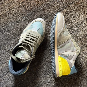Valentino Rockrunner i camouflage - Snygga Valentino Rockrunner sneakers i en cool kombination av grönt och gult med camouflage-mönster. Skorna har snörning och en unik design med färgglada detaljer på hälen. Perfekta för att ge din outfit en trendig touch.