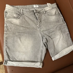 Grå jeansshorts från Only & Sons - Snygga grå jeansshorts från Only & Sons med klassisk femficksdesign. De har en normal passform och är perfekta för en avslappnad stil. Shortsen har en dragkedja och knapp framtill samt uppvikta benslut för en trendig look.