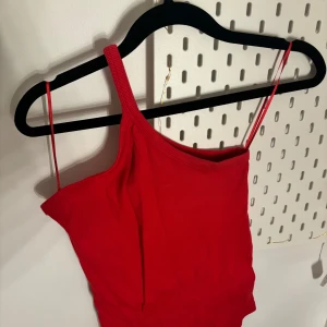 Röd oneshoulder topp - Snygg röd oneshoulder topp med smala axelband. Perfekt för en somrig look eller en utekväll. Enkel och stilren design som passar till många olika outfits.