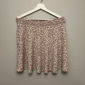 Blommig kortkjol i rosa  - Söt kortkjol i beige med ett blommigt mönster i vitt och svart. Kjolen har en elastisk midja för en bekväm passform. Perfekt för en dag på stranden eller finare tillställningar🫶🏼 köpt på Lager157 