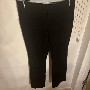 Svarta kostymbyxor - Snygga svarta kostymbyxor med en klassisk design. De har en rak passform och är perfekta för en stilren look. Byxorna har en diskret dragkedja och knappar framtill.