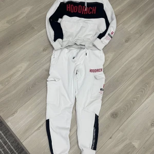 Hoodrich tracksuit - Snygg tracksuit från Hoodrich med svarta detaljer och röd logga. Byxorna har flera praktiska fickor och en modern design. Perfekta för en avslappnad stil.