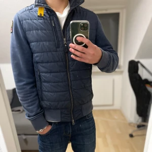 Blå jacka från Parajumpers - Säljer en snygg blå jacka/cardigan från Parajumpers. Perfekt för kyligare dagar med sin fleece och puffer kombination. Det finns en liten fläck på vänster ärmen. Ny pris 4600kr