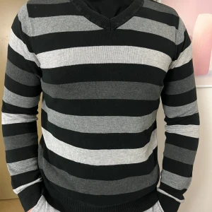 Svart och grå randig tröja - Snygg svart och grå randig tröja med v-ringning. Perfekt för en stilren look. Tröjan har långa ärmar och är gjord i ett mjukt material.