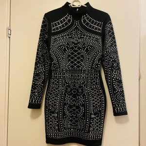 Svart klänning med paljetter - Snygg svart klänning med glittrande paljetter i ett detaljerat mönster. Klänningen har långa ärmar och en tight passform som framhäver figuren. Perfekt för en kväll ute eller en speciell tillställning.