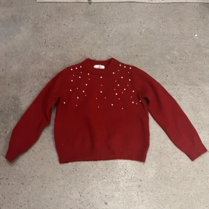 Röd stickad tröja med pärlor från H&M strl 134/140 - En röd stickad tröja från H&M dekorerad med pärlor på framsidan. Tröjan har långa ärmar och en rund halsringning. Perfekt för kyligare dagar och ger en stilren look.