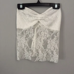 Vit spetstopp från Shein - Säljer en elegant vita spetstopp från Shein i storlek XS. Toppen har ett vackert blommigt mönster och en söt knytning baktilll.