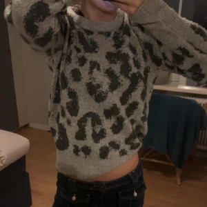 Grå leopardmönstrad stickad tröja - Säljer en snygg grå stickad tröja med leopardmönster. Tröjan har långa ärmar och en bekväm passform. Perfekt för att hålla sig varm och stilren.