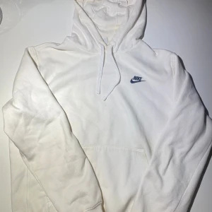 Vit hoodie från Nike - Säljer en stilren vit hoodie från Nike med klassisk logga på bröstet. Den har en justerbar huva och en stor magficka framtill. Perfekt för en avslappnad look.  Tröjan passar både M och L.