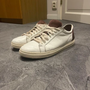 Vita sneakers med brun mocka - Snygga vita sneakers med bruna detaljer. Skorna är i läder och i bra skick. (Lite färgsläpp på ena tå) men inte något man tänker på. Nypris ca 1400. Strl 44. Från märket selected homme