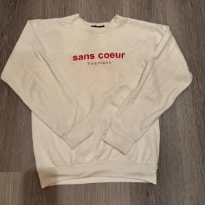 Vintage sweatshirt - Säljer en stilren vit sweatshirt med röd text 'sans coeur' på bröstet. Tröjan har långa ärmar och en klassisk rund halsringning. Perfekt för en avslappnad look.