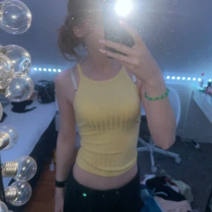 Gul ribbad linnetopp från Bershka - Säljer en snygg gul ribbad linnetopp från Bershka. Toppen är ärmlös och har en tight passform som framhäver figuren. Perfekt för varma sommardagar eller som ett lager under en jacka.