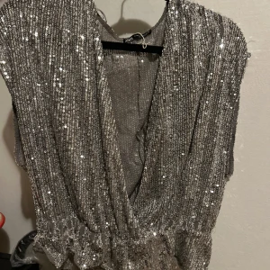 Glittrig silver topp - Säljer en glittrig silver topp med paljetter. Toppen har en djup v-ringning och är ärmlös, perfekt för festliga tillfällen.🤩🤩 Defekter: lite paljetter som är bort men inget jätte synligt. Passar oxå S