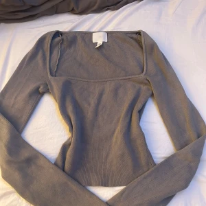 Grå ribbad topp - Säljer en stilren grå ribbad topp med långa ärmar och en fyrkantig halsringning. Toppen är croppad och passar perfekt för en trendig look. Perfekt för både vardag och speciella tillfällen.