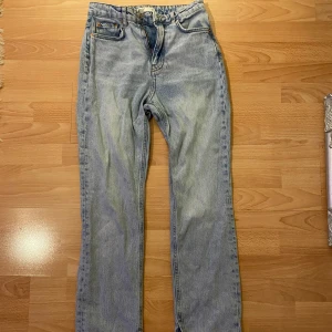Gina Tricot Blå jeans med slits  - Säljer ett par klassiska blå jeans från Perfect Jeans. De har en straight passform och är högmidjade med en dragkedja och knapp framtill. Jeansen har en sliten look med fransade kanter vid bensluten. Perfekta för en avslappnad stil.