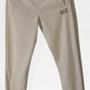 Vita byxor från Emporio Armani - Snygga beige byxor från Emporio Armani med EA7-logga på låret. Byxorna har en modern design med smal passform och är perfekta för en stilren look. De har fickor framtill och är tillverkade i ett mjukt material för extra komfort. 