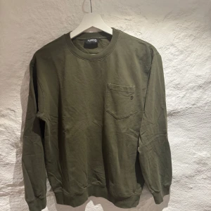 Olivgrön tröja från Dondup - Säljer en stilren olivgrön tröja från Dondup. Tröjan har en bröstficka och rund halsringning.  Den är i  bra skick och den har bara anvädts varsamt, pris kan diskuteras och var nu inte rädd att höra av dig vid några funderingar!🤩🍸🍾😉