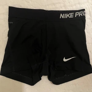 Nike Pro träningsshorts - Snygga svarta träningsshorts från Nike Pro med en elastisk midja och vit logga. Perfekta för intensiva träningspass och ger en bekväm passform.