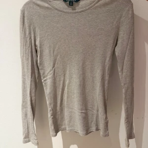 Grå långärmad tröja från Ralph Lauren - Säljer en stilren grå långärmad tröja från Ralph Lauren. Tröjan har en diskret broderad logga på bröstet och är tillverkad i ett mjukt bomullsmaterial. Perfekt för en avslappnad och bekväm stil.