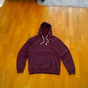 Vintage Vinröd Hoodie - Säljer en vinröd hoodie med en stor ficka framtill och justerbara snören i huvan. Perfekt för kyliga dagar och en avslappnad stil. Passar bra till jeans eller mjukisbyxor. Hör av dig vid intresse!