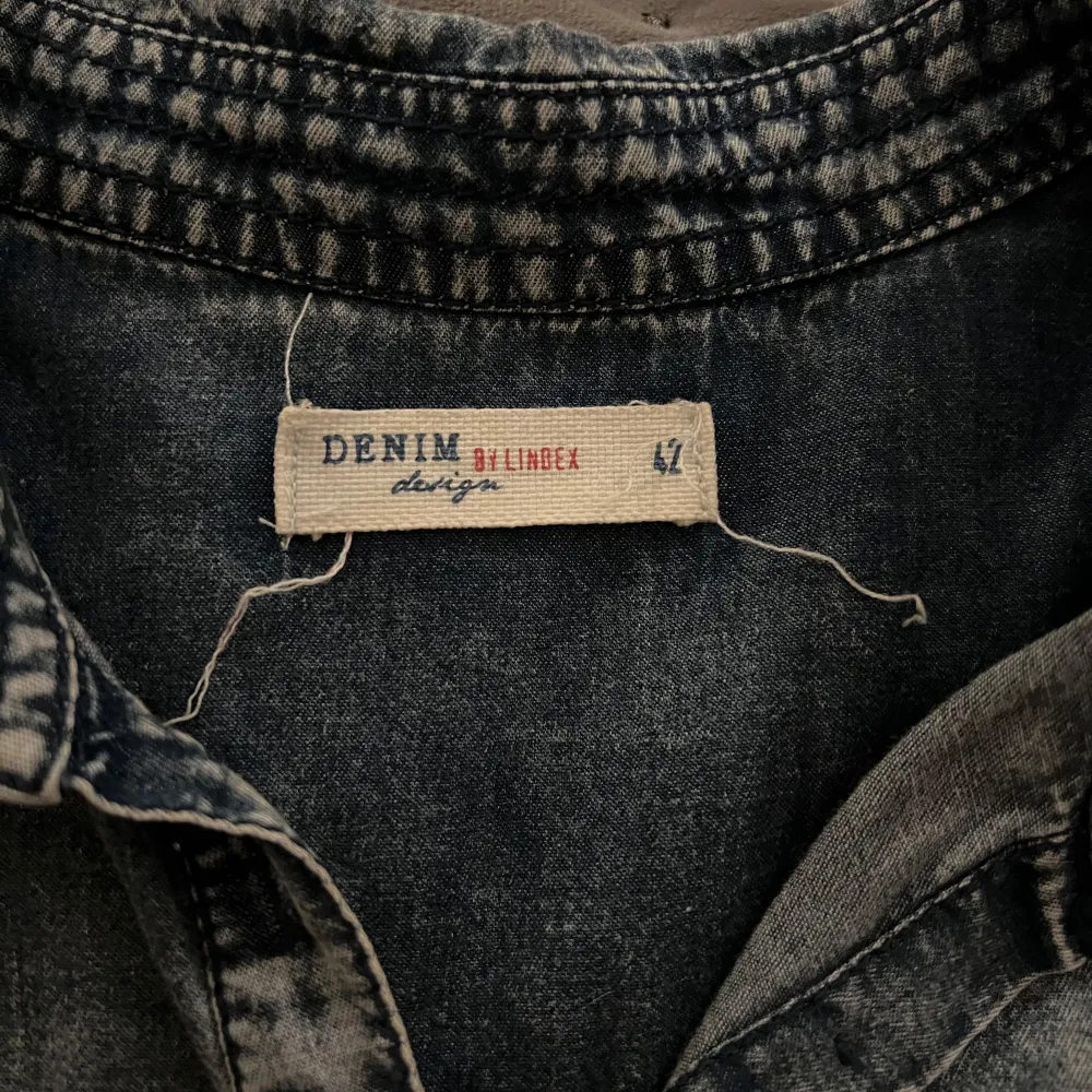 Snygg jeansskjorta/klänning från Denim by Linbex i storlek L. Skjortan har långa ärmar och två bröstfickor med knappar. Perfekt för en avslappnad stil med en klassisk denimlook.. Mekot.