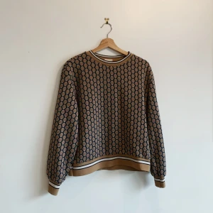 Mönstrad tröja från H&M x GP & J Baker - Säljer en unik tröja från H&M:s samarbete med GP & J Baker. Tröjan har ett geometriskt mönster i beige och svart med glittriga detaljer. Rund halsringning med randig kant och långa ärmar. Perfekt för att sticka ut med stil!