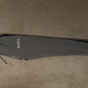 Grå mjukisbyxor från Hoodrich - Snygga grå mjukisbyxor från Hoodrich med elastisk midja och svarta detaljer längs sidorna. Tröjan till dessa byxor finns. Köp båda för bättre pris. Logotypen 'Hoodrich' är tryckt längs benet och på sidan.