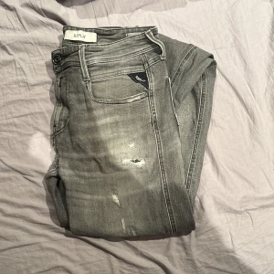 Replay anbass aged 10 y - Snygga grå jeans från Replay med slitna detaljer för en trendig look. Dom är aged 10 y därför lite dyrare. Det står 29 i midjan men mer som 30 - 31. längden är 34. Modellen är replay anbass slim fit. Pris ej hugget i sten. Litet hål mellan benen men absolut inget problem.